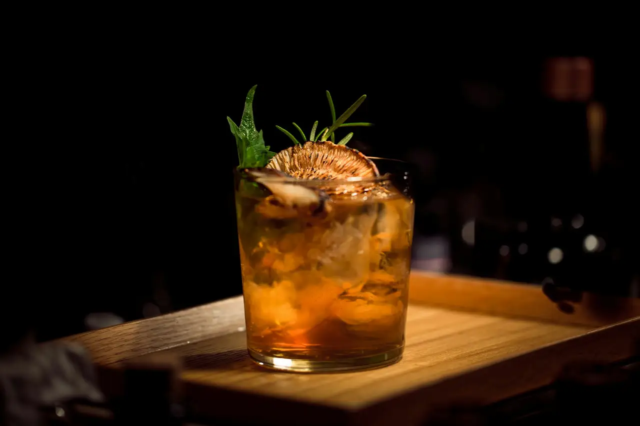 Un cocktail ambré sur un comptoir en bois, éclairé à la bougie